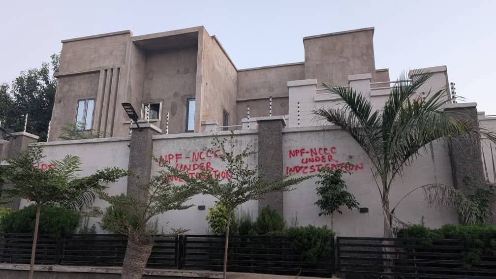 IMG_6092 - THEWILL NEWS MEDIA A modern concrete house with a high wall and a palm tree in front; red graffiti on the wall suggesting something about an investigation.