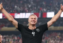 W’Cup: Haaland’s Brace Fires Norway Into Knockout Stage After Thrilling Win Over Senegal Soccer player with blond hair and a black jersey with number 9 raises arms in celebration on the field, crowd cheering in the stands.