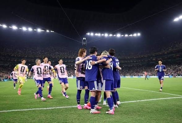 IMG_6602 Soccer players in blue uniforms celebrate with a group hug on a brightly lit stadium pitch at night.