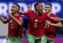 W’Cup: Morocco Stage Stunning Comeback in 4–2 Thriller Against Haiti Three Morocco football players celebrate a goal, wearing red jerseys and green shorts, arms raised in jubilation on the field with numbers 11, 9, and 23 visible.