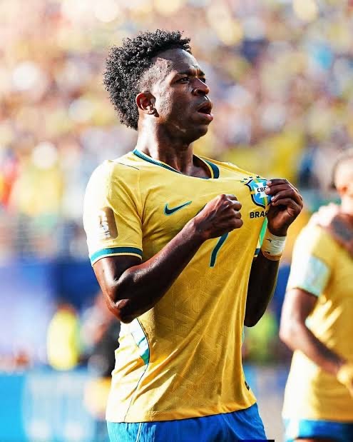 Brazilian soccer player in a yellow jersey cheers on the field, pulling at his shirt in celebration.