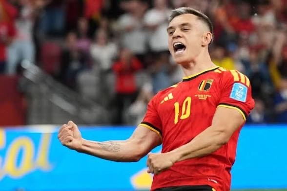 Trossard Belgian national team soccer player in a red jersey #10 celebrating with a fist pump on the field; stadium crowd in background.