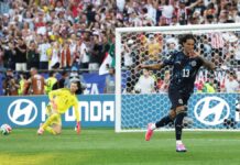 Paraguay Shock Germany On Penalties To Reach World Cup Round Of 16 Soccer scene: a player in a dark blue jersey #13 celebrates near the goal as the yellow-clad goalkeeper kneels on the pitch; a full stands crowd cheers behind them.