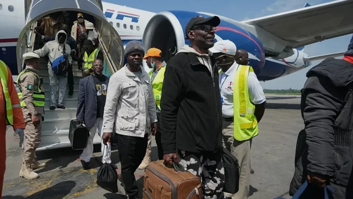 Nigerians-Return-From-South-Africa Group of passengers and crew disembarking a parked airplane via stairs, some wearing reflective vests and carrying luggage.