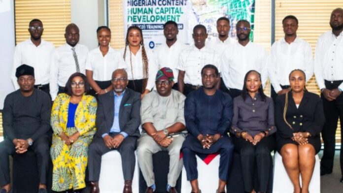 Oil-and-Gas-Field-Readiness_-NCDMB-Chevron-Bristow-Begin-Pilot-Training Group of professionals in business attire posing for a formal group photo in an office, with a Nigerian Content Human Capital Development banner in the background.