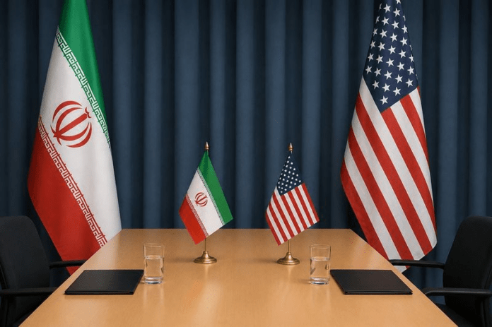 US-Iran Diplomatic conference table with Iranian and American flags, two small flags, notebooks, and water glasses against a dark curtain backdrop.