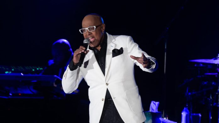 YGLS64G7UJHXFG2HOAYXHBUI6A Male singer in a white blazer and black shirt performs on stage, holding a microphone and gesturing energetically.
