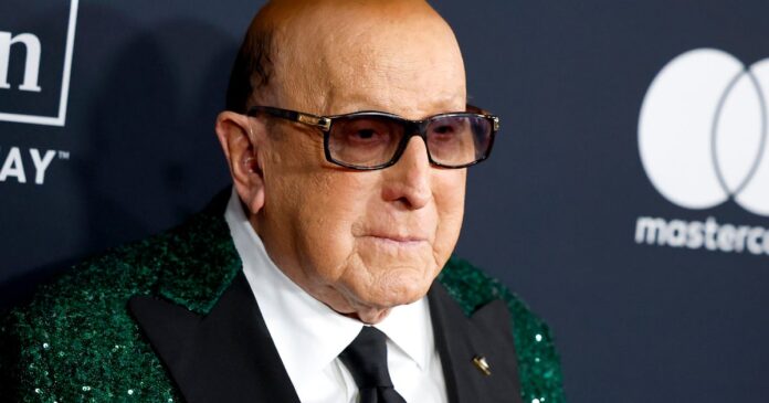 gettyimages-2259328694 Older man wearing dark sunglasses and a green sequined blazer at a formal event, neutral backdrop with logos behind him
