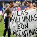 Banner That Could Land Argentina In Trouble Before World Cup Final Two shirtless soccer players hold a white banner that reads 'LAS MALVINAS SON ARGENTINAS' on a green field.