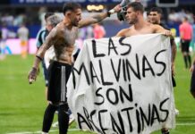 Banner That Could Land Argentina In Trouble Before World Cup Final Two shirtless soccer players hold a white banner that reads 'LAS MALVINAS SON ARGENTINAS' on a green field.