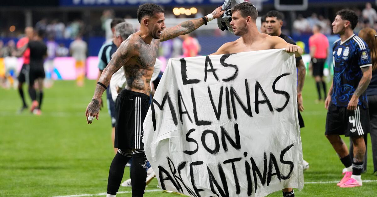 Two shirtless soccer players hold a white banner that reads 'LAS MALVINAS SON ARGENTINAS' on a green field.