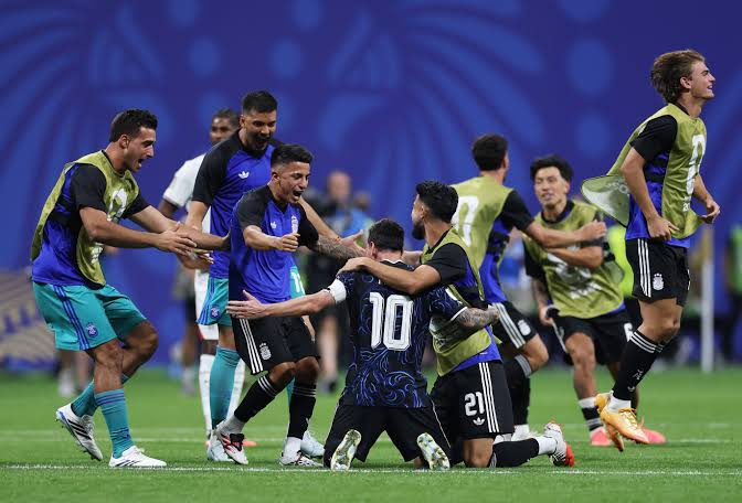 Soccer players in blue and black jerseys celebrate on the field with high-fives and embraces.