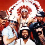 Village People Lead Singer Victor Willis Dies At 74 Six men in colorful 70s‑80s costumes posing together against a red background, including a cowboy, construction worker, Native American chief, biker, and sailor.