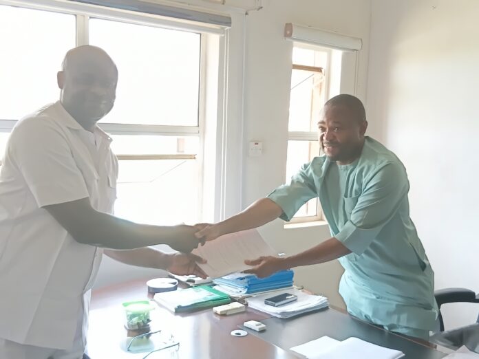 20260630_132711 Two healthcare workers in an office shake hands over a desk full of paperwork and folders.
