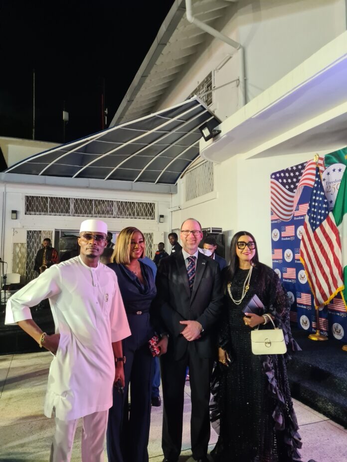 Group of formally dressed people posing for a photo at an event with US flags and a 'Freedom 250' backdrop at night