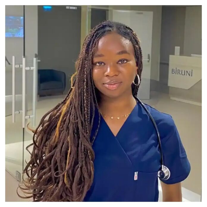 23-year-old-Nigerian-medical-doctor-Adaobi-Nnani Portrait of a healthcare professional with long braided hair, wearing navy scrubs and a stethoscope, standing in a modern clinic lobby.