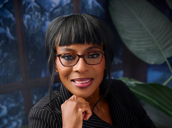 Bolaji Odusina Portrait of a smiling woman with short black hair and glasses, resting her chin on her hand in a professional setting.