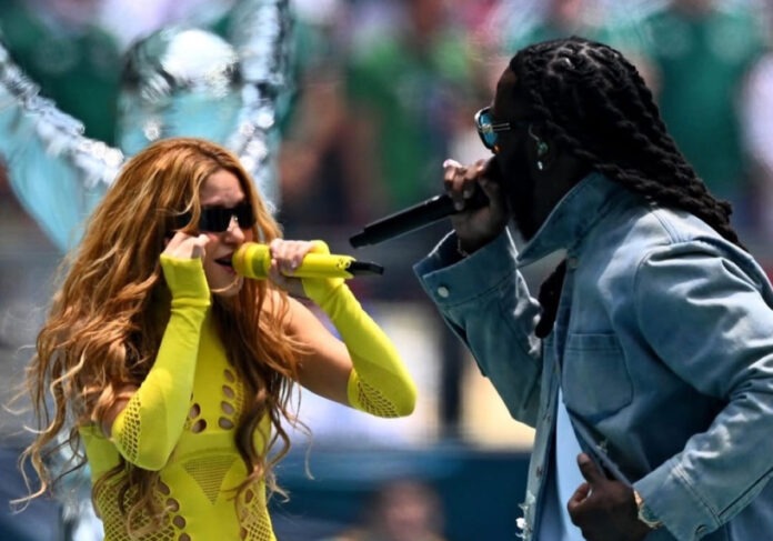 Burna Boy and Shakira performing live at the Estadio Azteca in Mexico City, Mexico, during the 2026 FIFA World Cup opening ceremony, on June 11, 2026. Photo Credit: afrika.world via Instagram) Two performers sing into wireless mics on an outdoor stage; woman in neon yellow cutout bodysuit beside a man with dreadlocks.