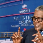 Marketers Reject Dangote’s Dollar Fuel Pricing, Warn Of FX Pressure And Higher Pump Prices Man in a dark suit and glasses making a two-handed gesture while speaking, with a large blue Dangote crude oil tank in the background.