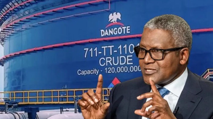 Dangote & Dollar Pricng Man in a dark suit and glasses making a two-handed gesture while speaking, with a large blue Dangote crude oil tank in the background.