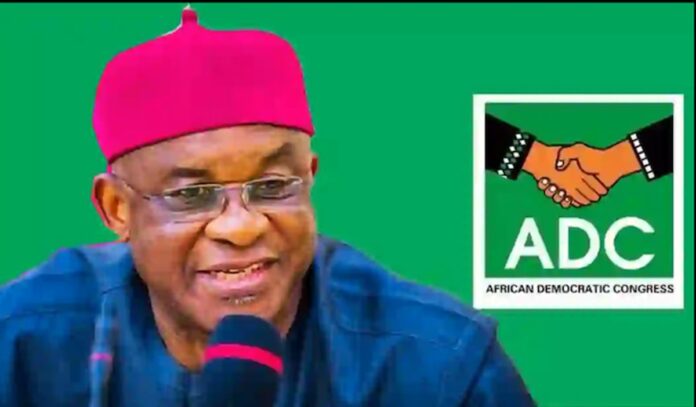 Portrait of a man in a pink cap speaking into a microphone, with an ADC (African Democratic Congress) logo on a green background.