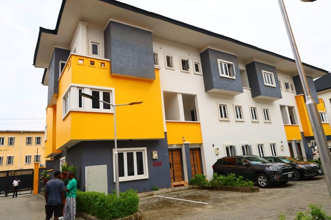 EFCC secured a final forfeiture judgement of 52 luxury terrace and maisonette units - THEWILL NEWS MEDIA Colorful modern apartment building with yellow and gray façades, parked cars, and people near the entrance.