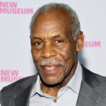 Danny Glover Reveals Alzheimer’s Diagnosis Portrait of an older Black man in a gray suit at a New Museum event backdrop with pink logos in the background