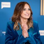 Actress Mariska Hargitay to Host 2026 Emmy Awards as First Woman in 15 Years Smiling woman in a blue velvet blazer with hands pressed together in a greeting against a blue event backdrop.