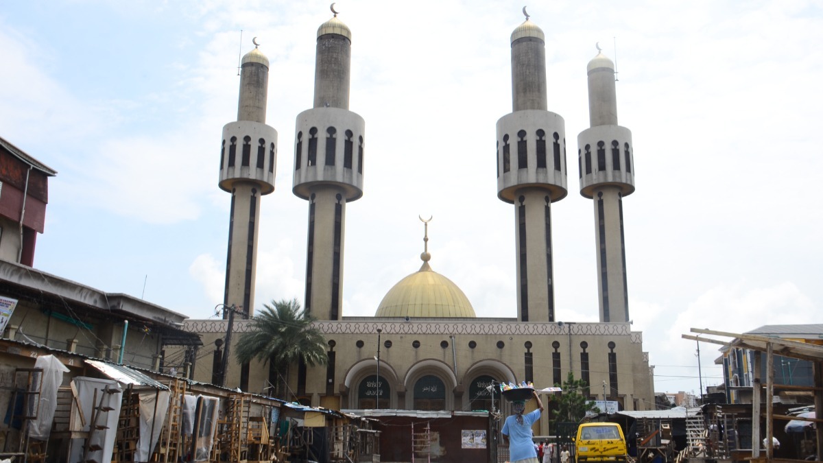 The Lagos Island Central Mosque - THEWILL NEWS MEDIA Mosque with four tall minarets and a gold dome, viewed from a busy street market in front of it.