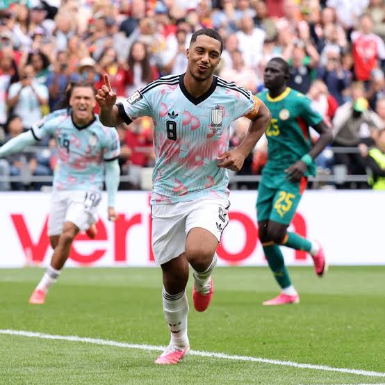 Footballer in a light blue kit (#8) celebrates a goal, sprinting toward the camera on a crowded pitch.