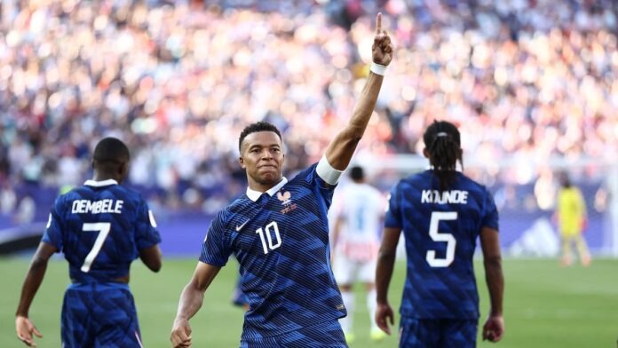 Kylian Mbappe Soccer player in blue with number 10 raises his right arm in celebration on the field, flanked by teammates wearing numbers 7 and 5.