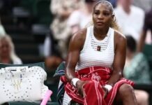 Serena Williams Withdraws From Wimbledon Doubles Over Knee Injury Serena Williams sits courtside on a bench, wearing a white sleeveless top and holding a red towel, with a white studded bag beside her.