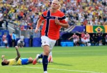 Haaland’s Late Double Sends Norway Past Brazil Into Historic World Cup Quarter-Finals Norwegian soccer player in red jersey runs on the field while a teammate lies on the grass and spectators cheer in the stands Behind them, a Brazilian flag banner is visible.