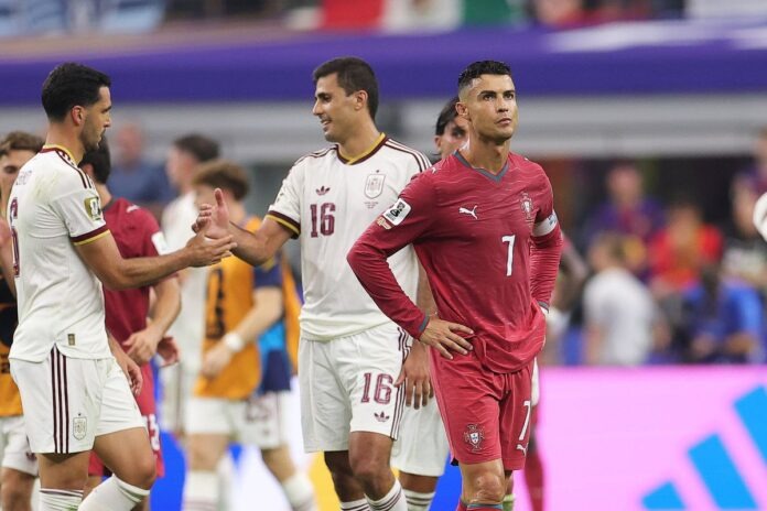 Spain Break Portugal Hearts Ronaldo Portugal player in red jersey #7 stands with hands on hips as teammates in white uniforms shake hands in the background at a stadium.