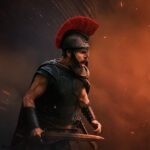 Christopher Nolan’s “The Odyssey” Earns Positive First Reactions from Critics Roman warrior in black armor with a red-plumed helmet readies a sword amid fiery smoke and sparks on a battlefield scene