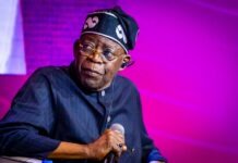Tinubu Orders EFCC to Unfreeze Osun Account Male performer on stage, wearing a dark pinstripe outfit and a head wrap, holding a microphone under purple lighting