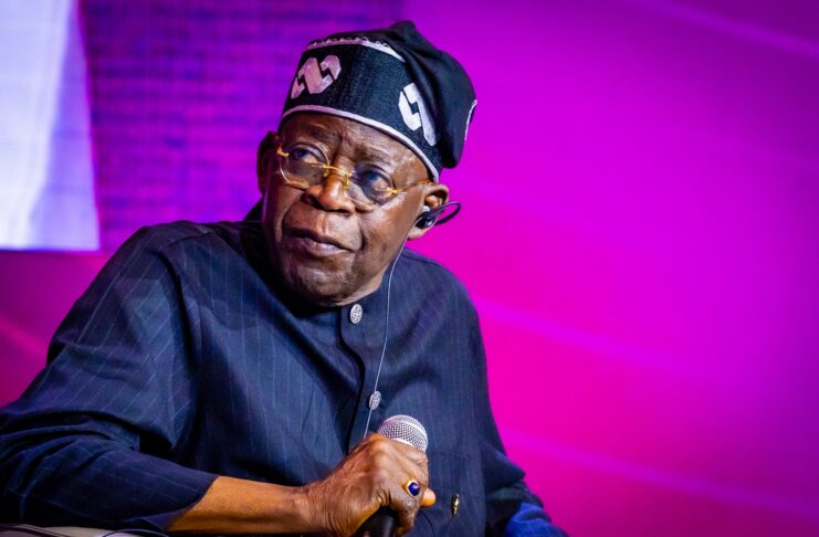 Tinubu Orders EFCC to Unfreeze Osun Account Male performer on stage, wearing a dark pinstripe outfit and a head wrap, holding a microphone under purple lighting