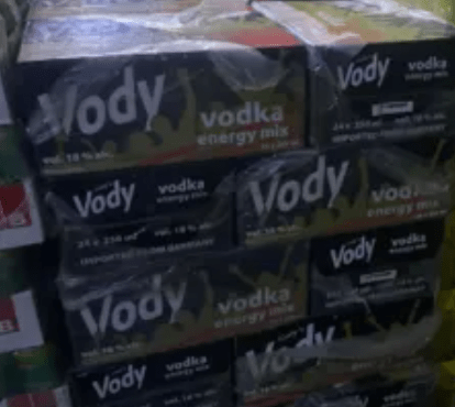Stack of Vody vodka energy mix boxes on a store shelf, dark blue and yellow packaging.