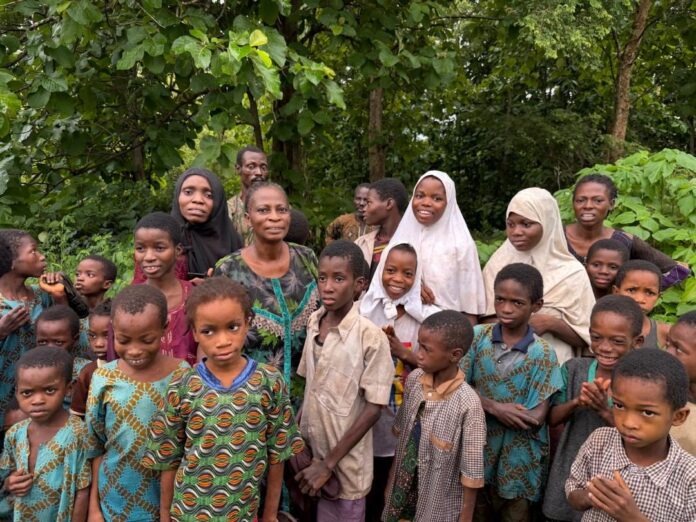Group of African children and women standing together outdoors in a green, forested area.