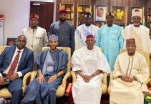 2027: Gov Yusuf Inaugurates Committee To Draft Campaign Blueprint Group of nine men in traditional and formal attire posing for a photo in an office setting, some seated in chairs and others standing behind them.