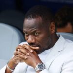 Senegal Sack Pape Thiaw After World Cup Exit Black man in a light blazer seated with hands folded near his lips, looking contemplative.