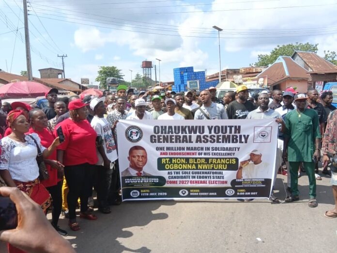 Crowd of young people marching on a street holding a large banner for Ohaukwu Youth General Assembly political rally in Ebonyi State, Nigeria.