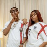 TikTok Stars Jarvis, Peller Set August 1 As Wedding Date Two people in England football jerseys pose indoors: the man with glasses makes a shushing gesture, the woman with long red hair rests her arm on his shoulder.