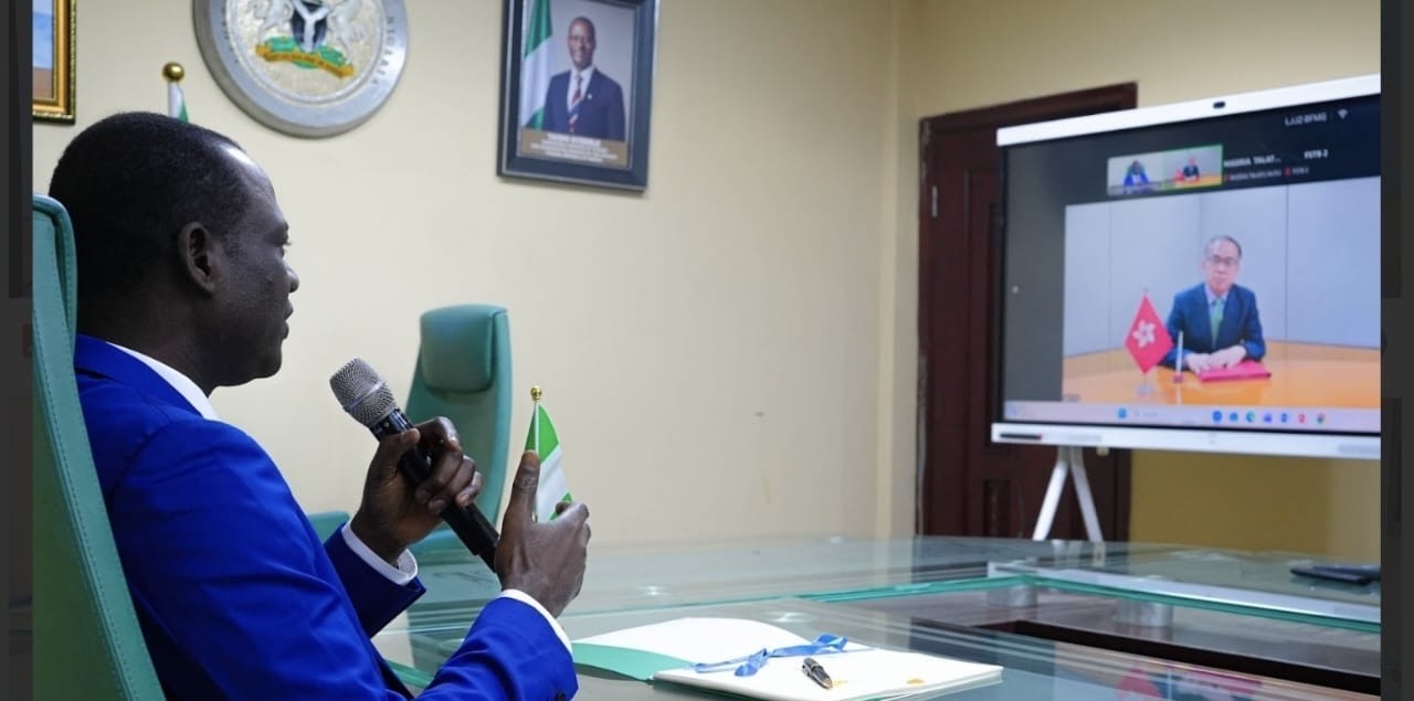 Nigeria’s Minister of Finance and Coordinating Minister of the Economy,. Taiwo Oyedele, and Hong Kong's Secretary for Financial Services and the Treasury, Christopher Hui during the signing of the agreement. - THEWILL NEWS MEDIA Man in a blue suit speaks into a handheld microphone during a virtual meeting, with a Nigerian flag on the desk and a video call on a large screen.