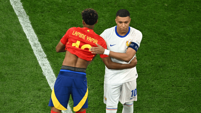 France's Kylian Mbappé and Spain's Lamine Yamal headline a blockbuster FIFA World Cup 2026 semifinal with a place in the final on the line. Two soccer players hug on a green pitch: one in a red jersey with 'LAMINE YAMAL' and number 10, the other in a white pinstriped kit with blue accents and a captain's armband.