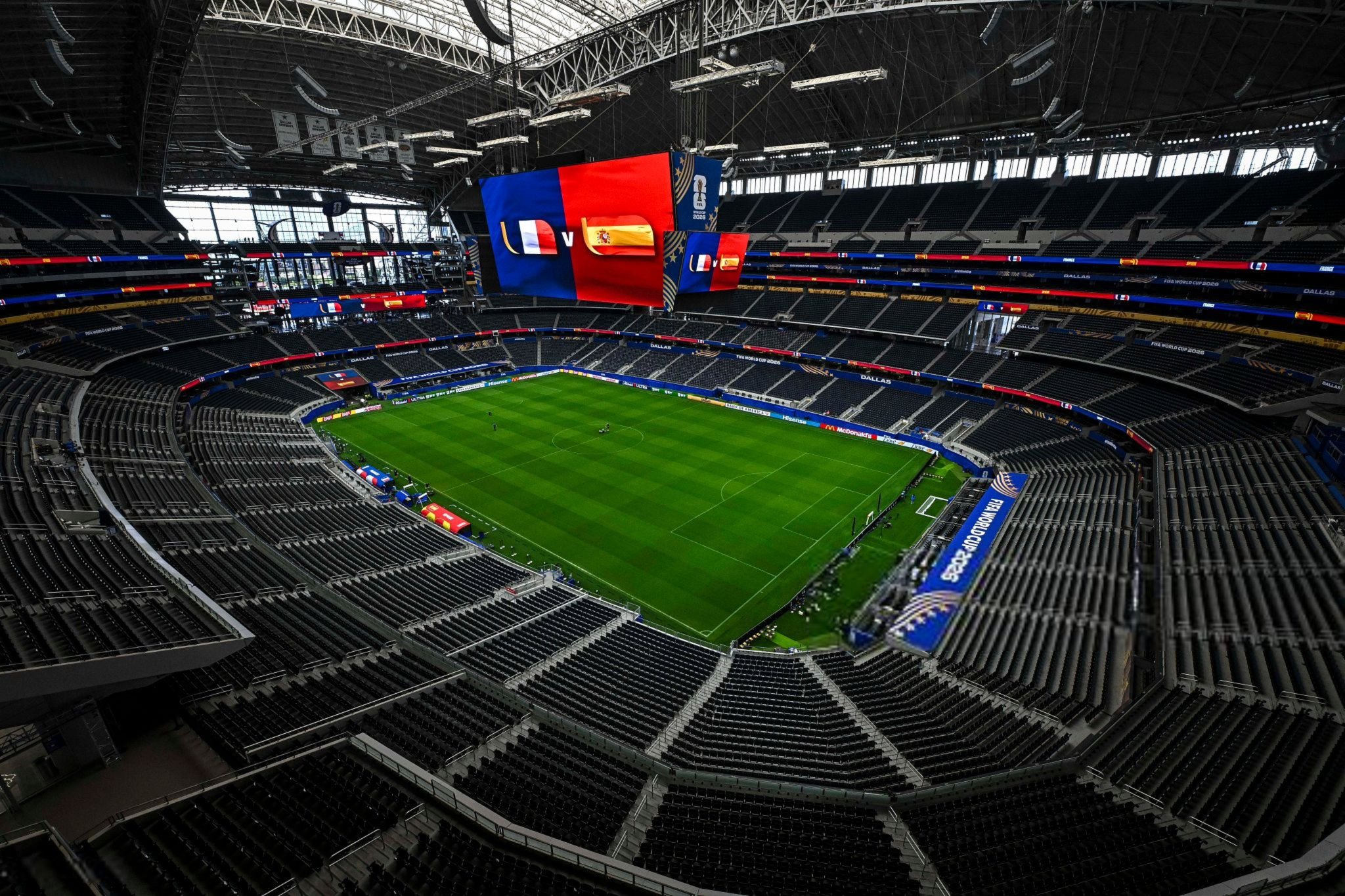 Dallas Stadium in Arlington, Texas, will host the eagerly anticipated FIFA World Cup 2026 semifinal between France and Spain. - THEWILL NEWS MEDIA Interior of a large football stadium with a green pitch and empty black seats, a massive hanging video screen displaying blue and red panels and flags above the field.