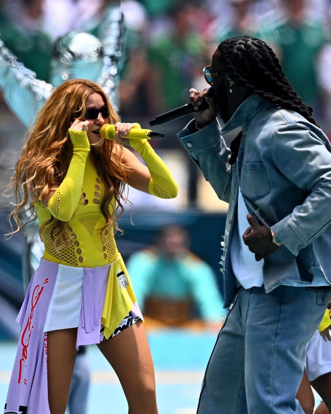 Burna Boy and Shakira performing live at the Estadio Azteca in Mexico City, Mexico, during the 2026 FIFA World Cup opening ceremony, on June 11, 2026. Photo Credit: afrika.world via Instagram) - THEWILL NEWS MEDIA Two musicians perform on a sunny stage: a woman in a neon yellow outfit singing into a yellow mic, facing a man in a light blue denim jacket who also holds a mic.
