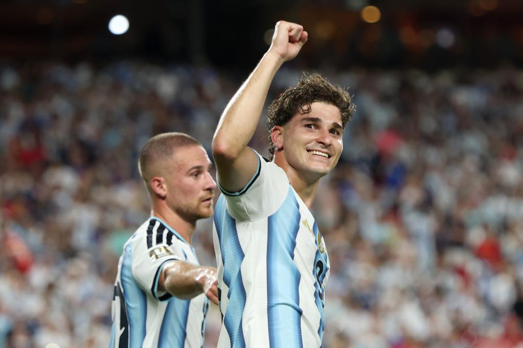 Julian Alvarez celebrates a goal - THEWILL NEWS MEDIA Two soccer players in light-blue-and-white Argentina jerseys celebrate on the field, one raising his fist in triumph as a cheering crowd looks on in the background.