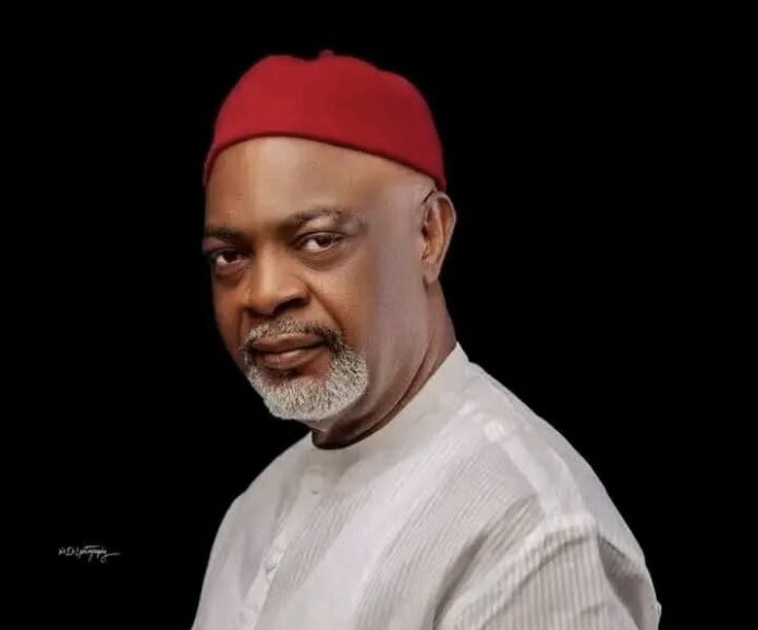 Portrait of a mature man wearing a red cap and white traditional outfit, posed against a black background.