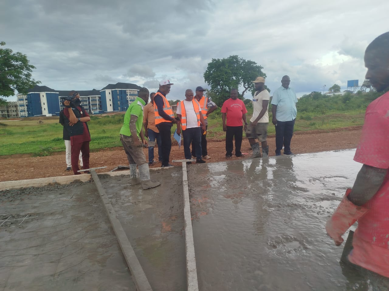 Group of workers and supervisors inspecting a freshly poured concrete slab at a construction site with muddy ground and cloudy sky.